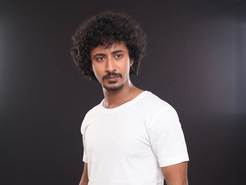 Portrait of a fashionable man in casual attire against a dark background, showcasing modern style.