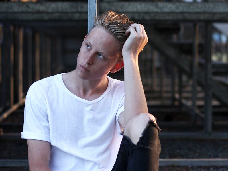 man sitting on floor wearing white crew-neck T-shirt