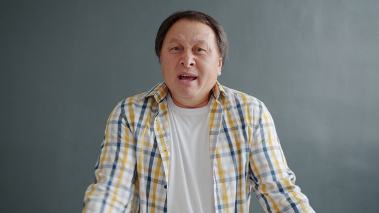 Man in plaid shirt speaking with open mouth.