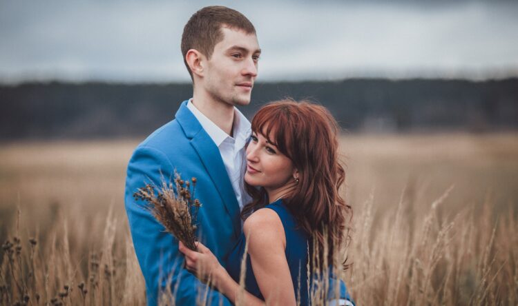 a man and woman standing in a field of tall grass