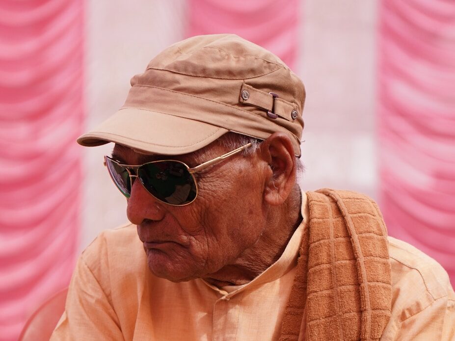 a man wearing a hat and sunglasses sitting in a chair
