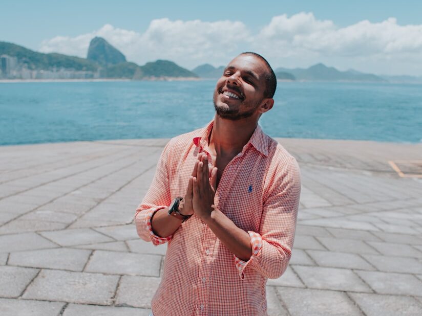man in pink dress shirt standing on gray concrete pavement near body of water during daytime