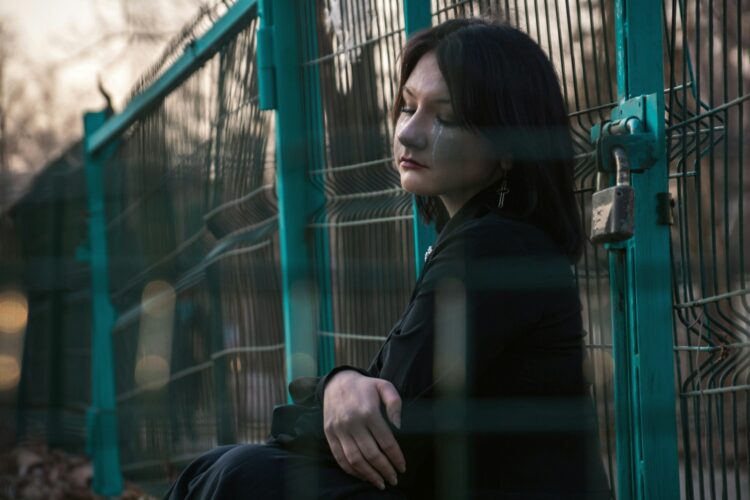 A woman leans against a fence with eyes closed.