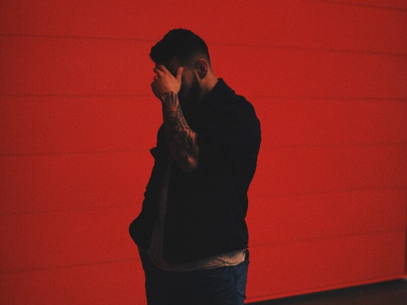 man in black long sleeve shirt and blue denim jeans standing beside orange wall