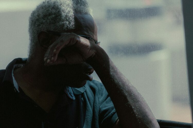 A man with silver hair covers his face.