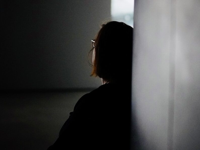a woman sitting in a dark room next to a wall