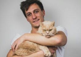 man in white crew neck t-shirt carrying brown cat