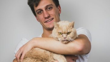 man in white crew neck t-shirt carrying brown cat