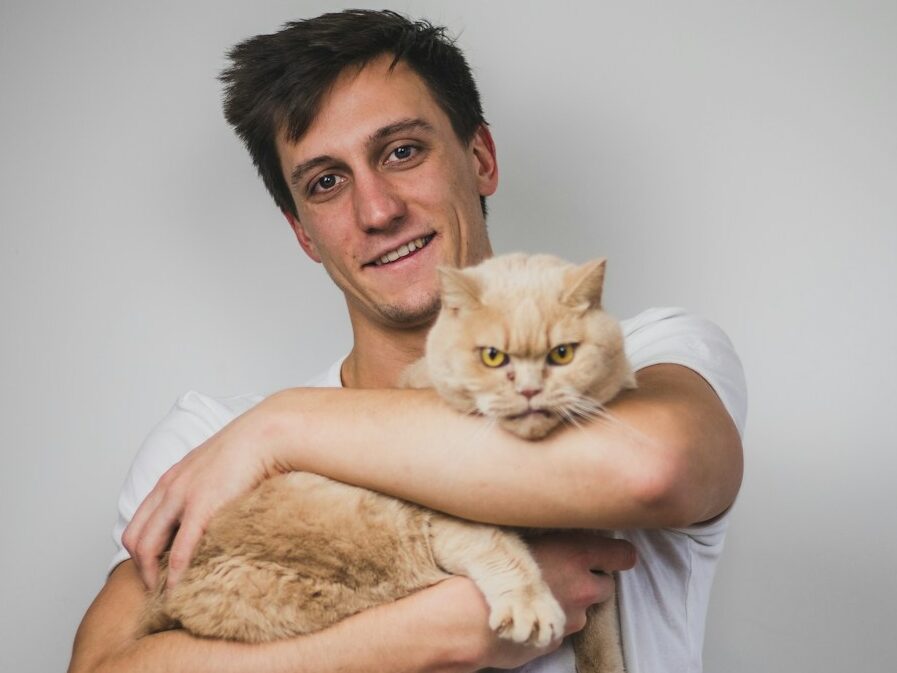 man in white crew neck t-shirt carrying brown cat