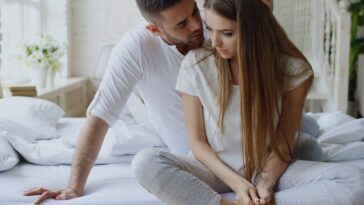 Couple sitting on a bed, man whispers to woman