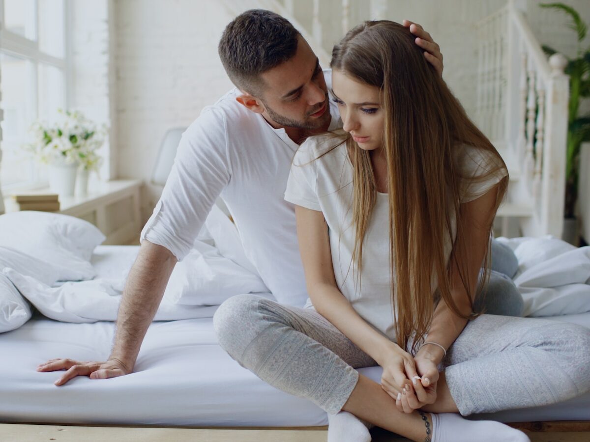 Couple sitting on a bed, man whispers to woman