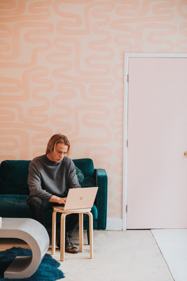 man in gray long sleeve shirt sitting on blue sofa working on a Microsoft Surface laptop
