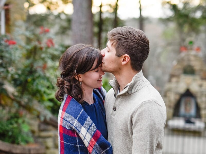 man kissing on woman forehead standing near tree during daytime