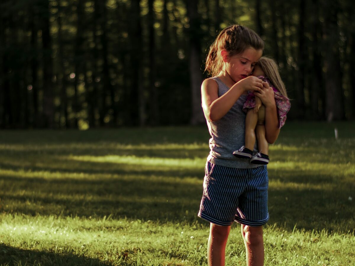 a little girl holding a stuffed animal in a field