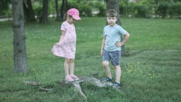 girl and boy standing beside trees during daytime