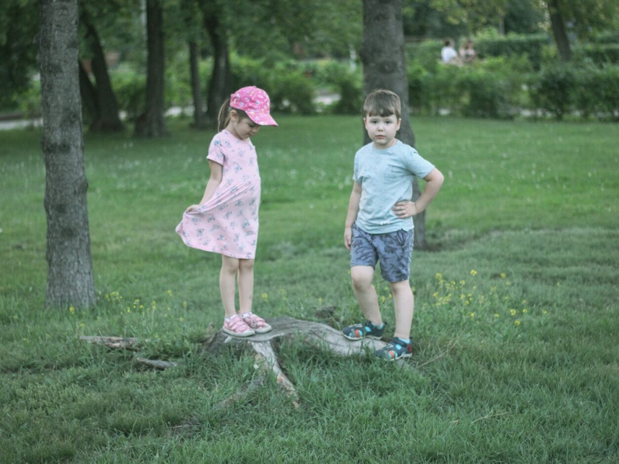 girl and boy standing beside trees during daytime