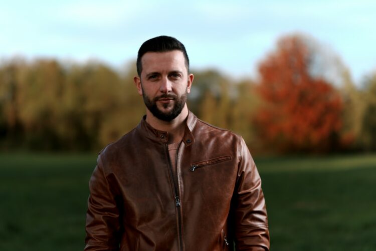 a man in a leather jacket standing in a field