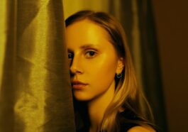 A woman standing behind a curtain in front of a window