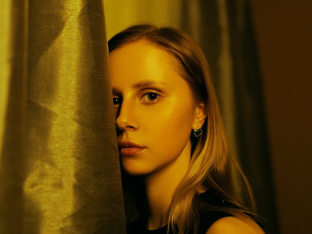 A woman standing behind a curtain in front of a window