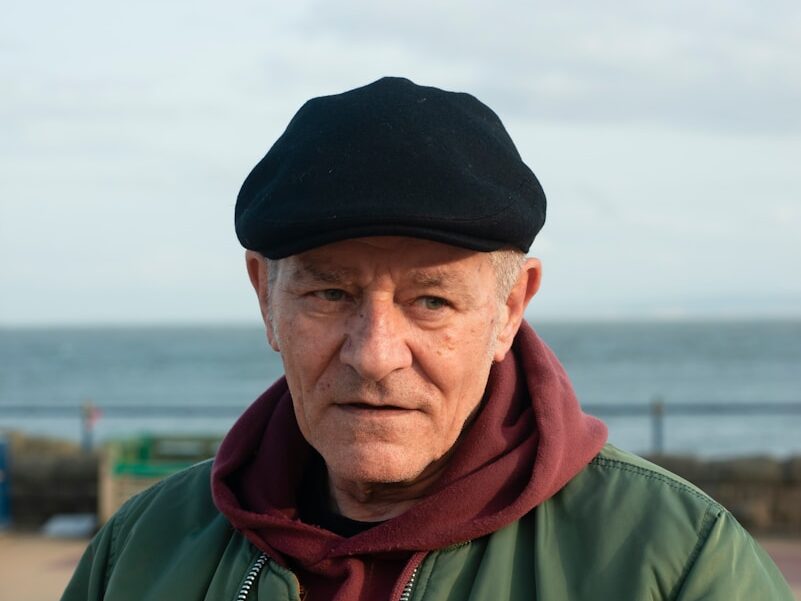 an old man wearing a black hat and a green jacket
