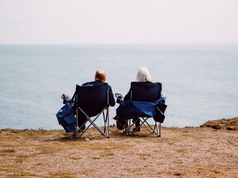 2 person sitting on blue camping chairs on brown field during daytime