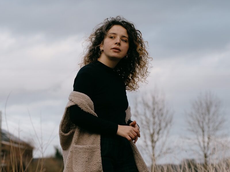 woman in black long sleeve shirt and gray scarf standing on grass field during daytime