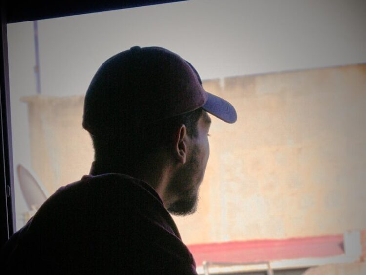 a man sitting in front of a window with a hat on