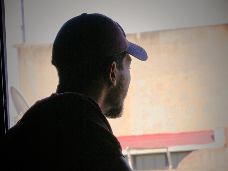 a man sitting in front of a window with a hat on
