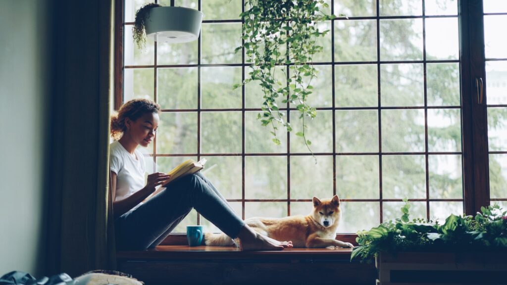 Woman reads a book near her dog.
