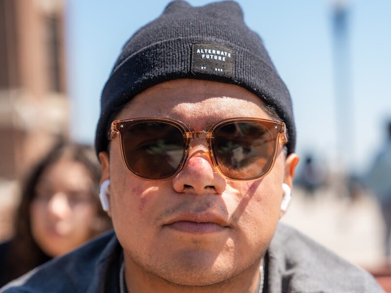 a man wearing sunglasses and a beanie looks at the camera
