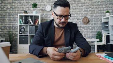 a man sitting at a table with a laptop and money