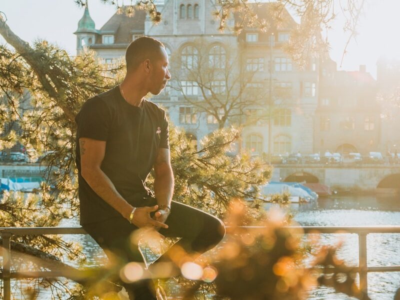 man sitting on metal railings beside the river