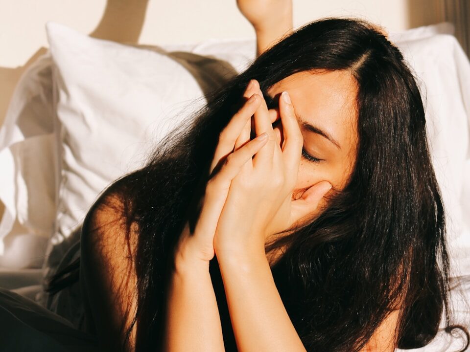 a woman laying in bed with her hands on her face