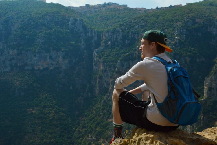 man in white long sleeve shirt and black pants sitting on rock mountain during daytime