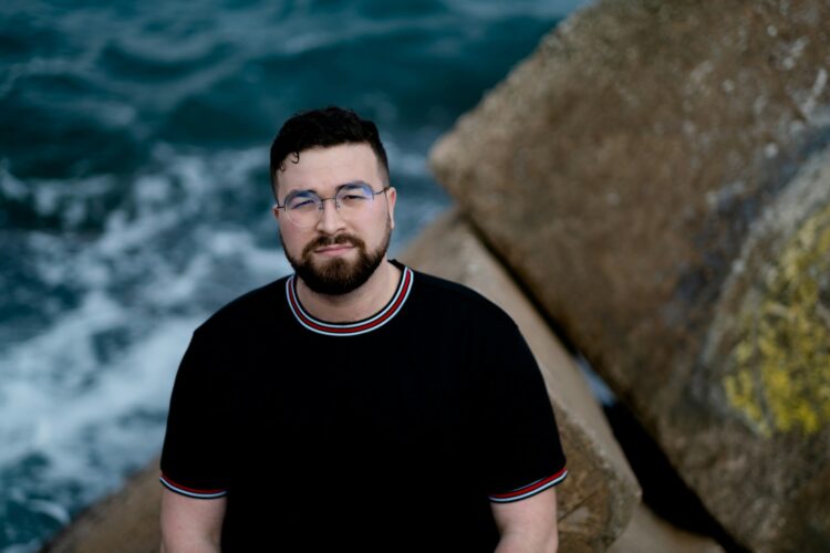 a man with glasses standing next to a body of water