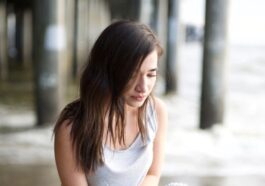 woman in white tank top and blue denim jeans sitting on concrete floor during daytime