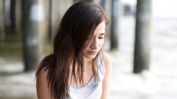 woman in white tank top and blue denim jeans sitting on concrete floor during daytime