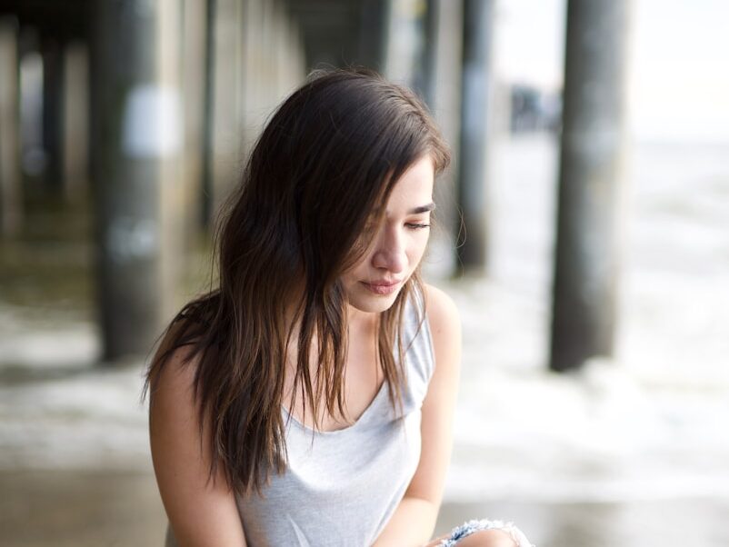 woman in white tank top and blue denim jeans sitting on concrete floor during daytime