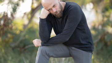man in black long sleeve shirt and gray pants sitting on green grass during daytime