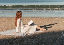 a woman sitting on a beach reading a book