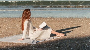 a woman sitting on a beach reading a book