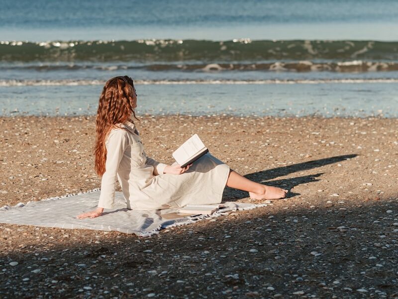 a woman sitting on a beach reading a book