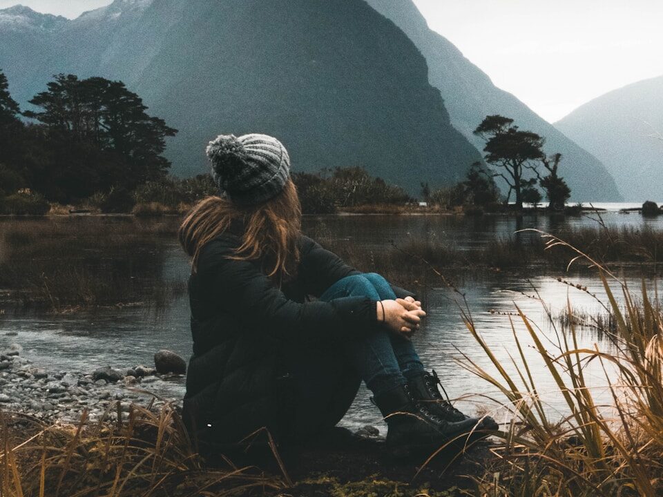 woman sitting near body of water looking at clouds