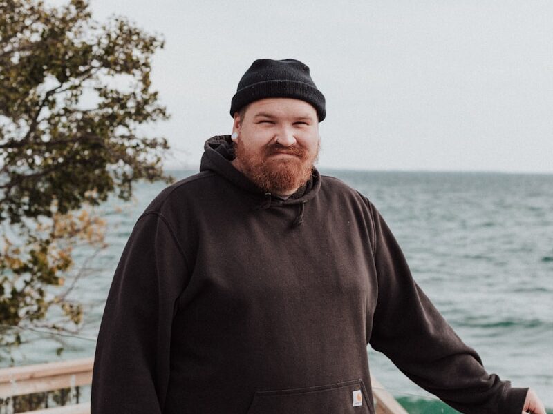 A man in a black hoodie standing on a wooden deck next to the ocean