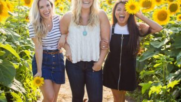 three women standing between sunflowers