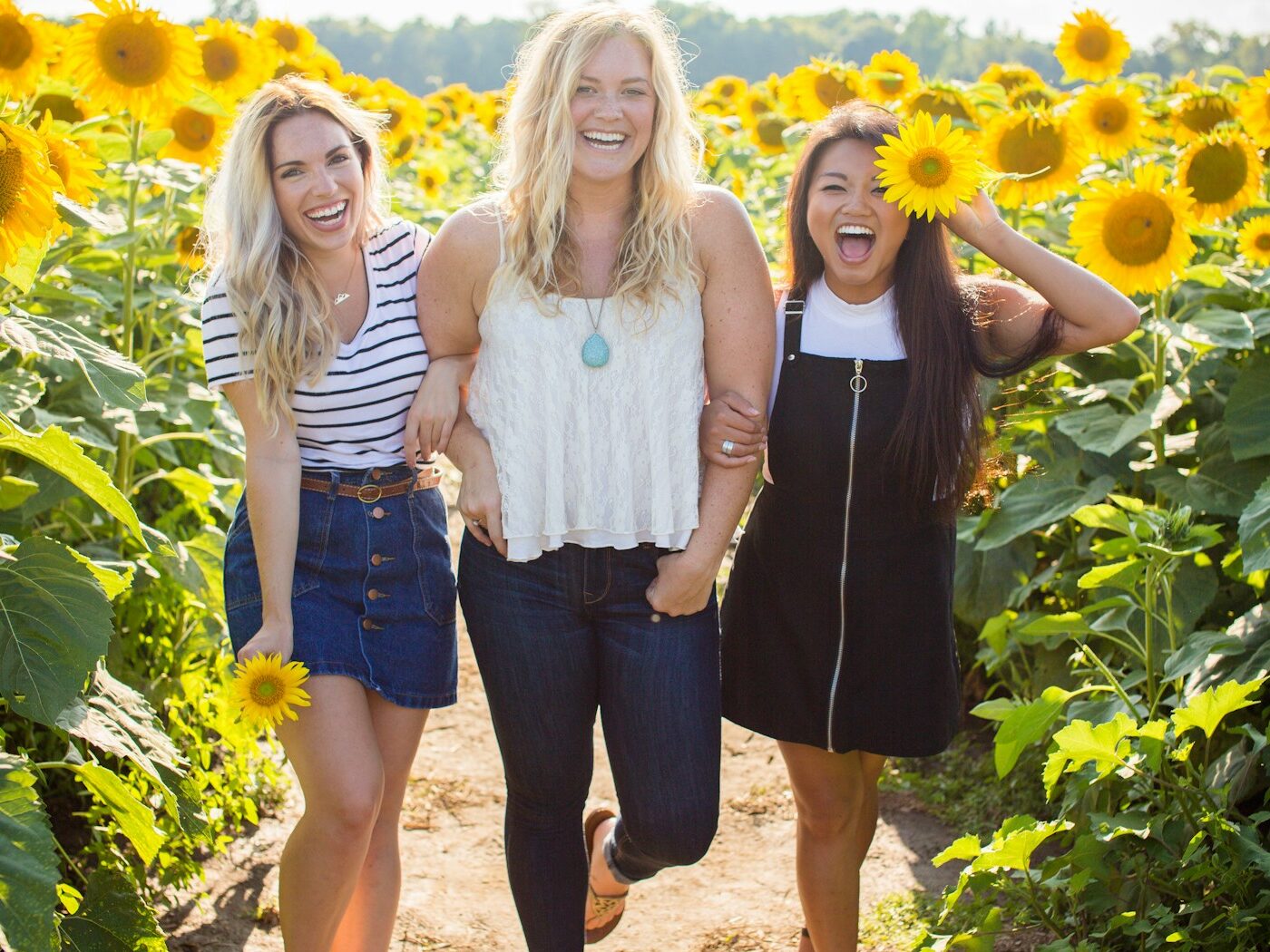 three women standing between sunflowers