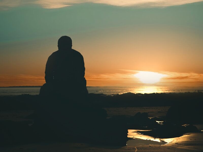 silhouette of man standing on seashore during sunset