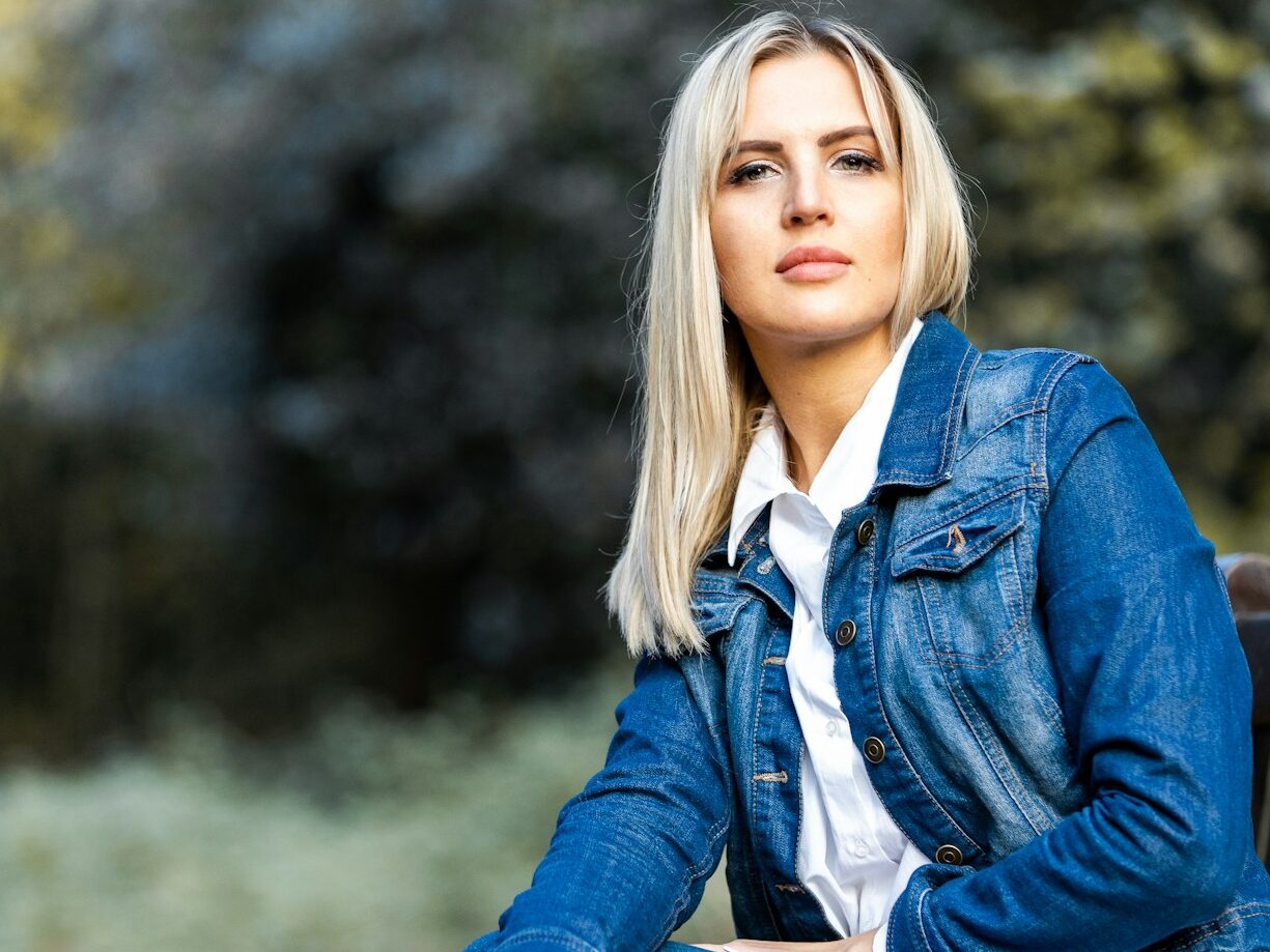 woman in blue denim jacket sitting on brown wooden bench during daytime