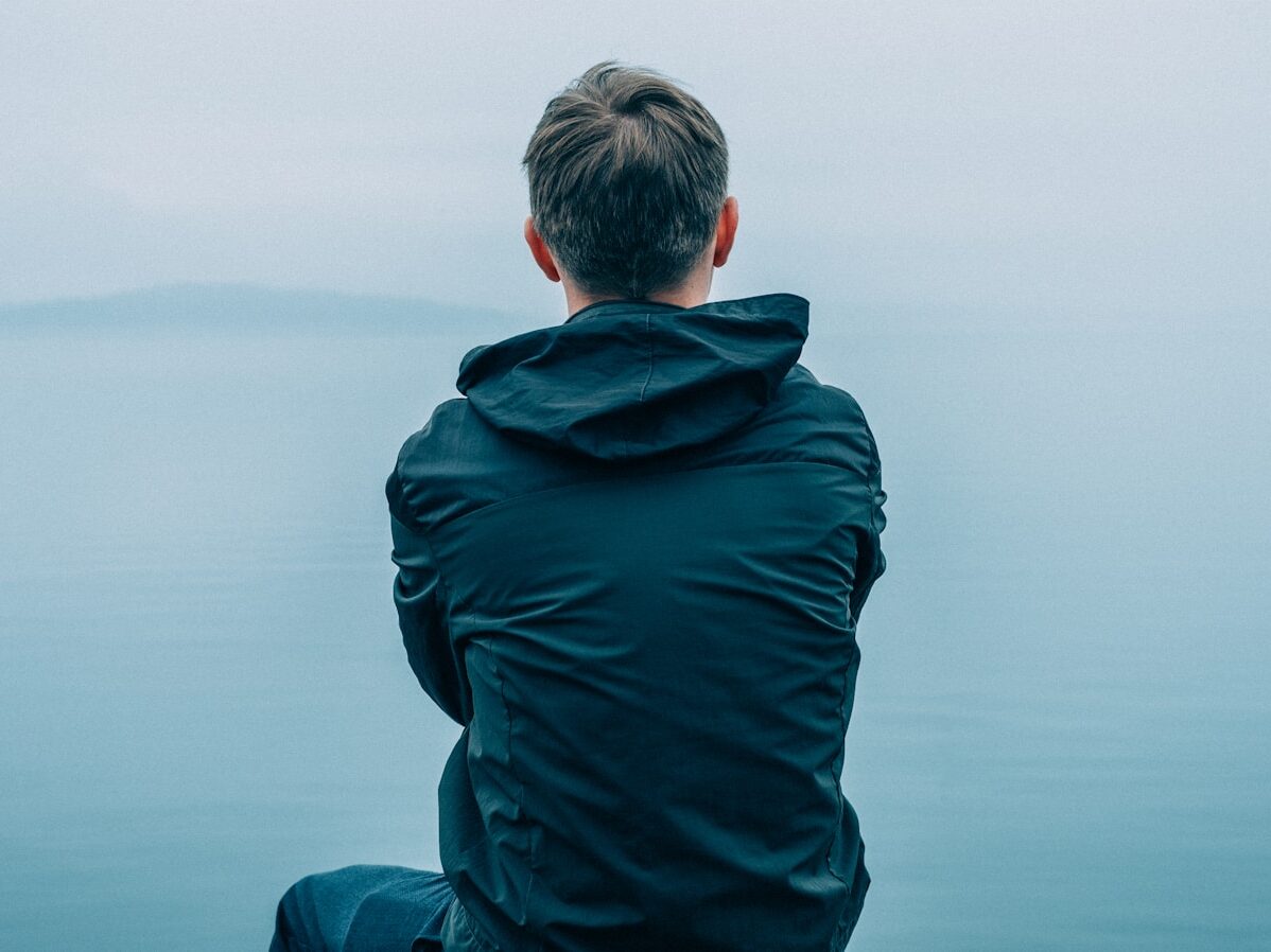 man in black hoodie sitting in front of ocean