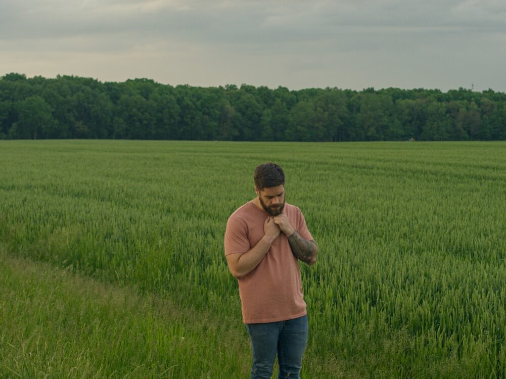 man in brown long sleeve shirt and blue denim jeans standing on green grass field during